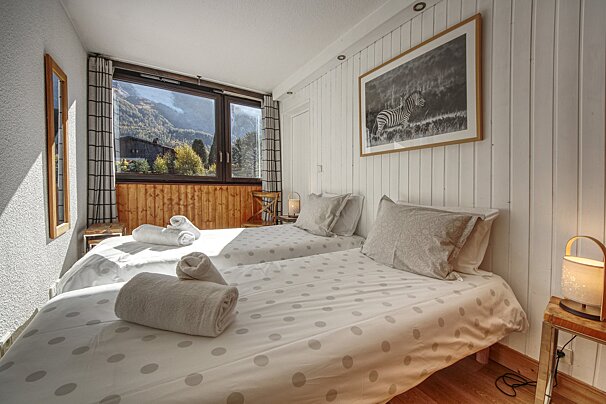 Cozy twin bedroom with polka dot bedding, wooden accents, and a large window offering a stunning mountain view. A zebra picture hangs on a white paneled wall.