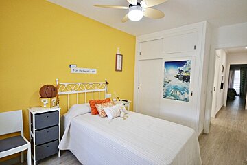 A bedroom with a yellow accent wall, a white bed, a ceiling fan, and sliding closet doors featuring a Zelda poster.