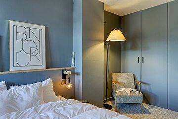 A modern bedroom featuring blue-grey walls, white bedding, a