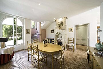 Rustic dining room features an oval table, ladder-back chairs, stone fireplace, arched windows, and herringbone tile floor.