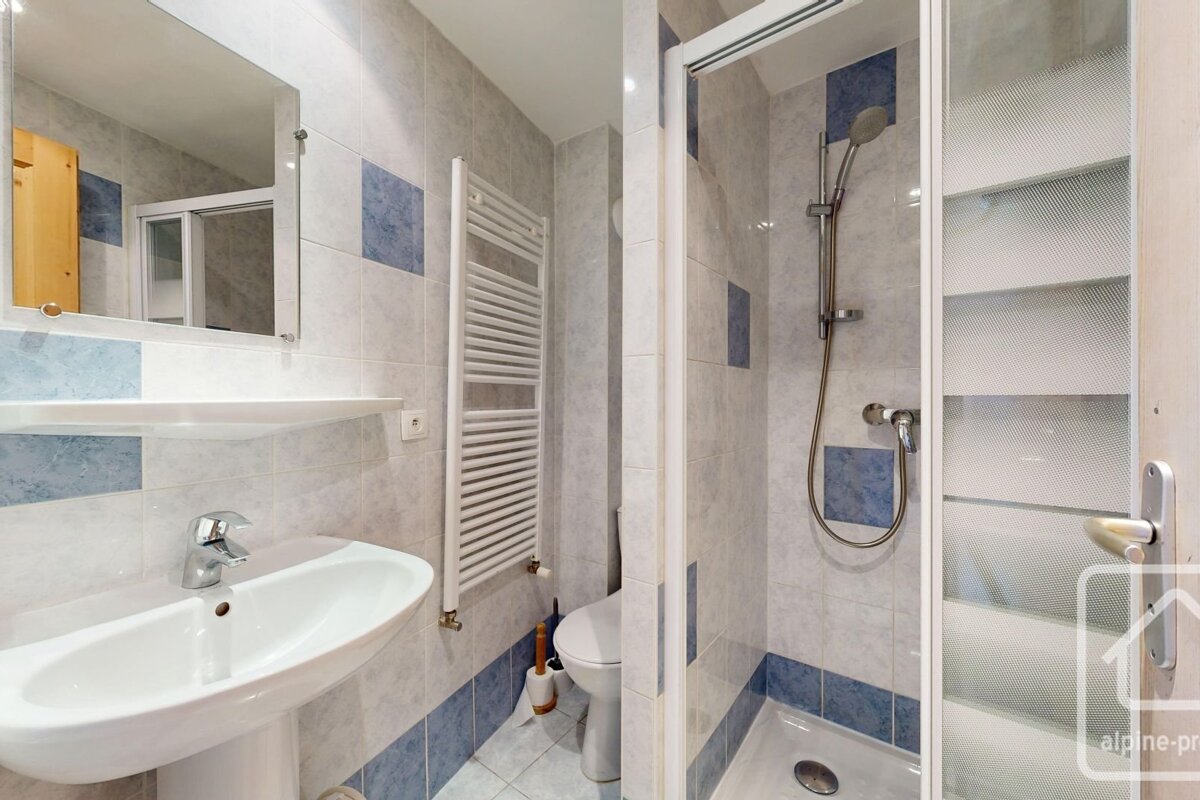 Tiled bathroom with a sink, mirror, towel warmer, toilet, and shower cabin. Features light blue and white/grey accent tiles.