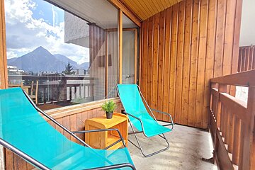 Two blue chairs sit on a balcony with mountains in the background