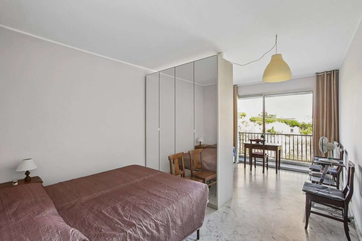 A modern bedroom with a large mirrored wardrobe separating the bed from a study area near a balcony.