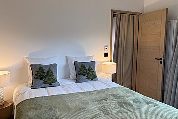Cozy bedroom featuring a bed with a green throw, pine tree pillows, warm bedside lamps, and a wooden door.