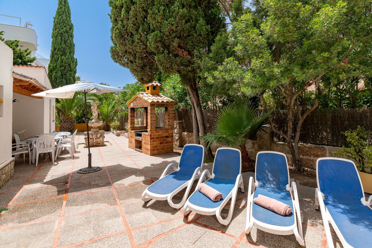 A patio with blue lounge chairs and a brick grill
