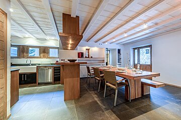 Modern rustic kitchen/dining room with wooden beams, dark tiled floors, and a long wooden table set for dinner.