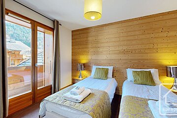 Cozy bedroom with wood-paneled wall, twin beds with green cushions, and a glass door opening to a balcony.