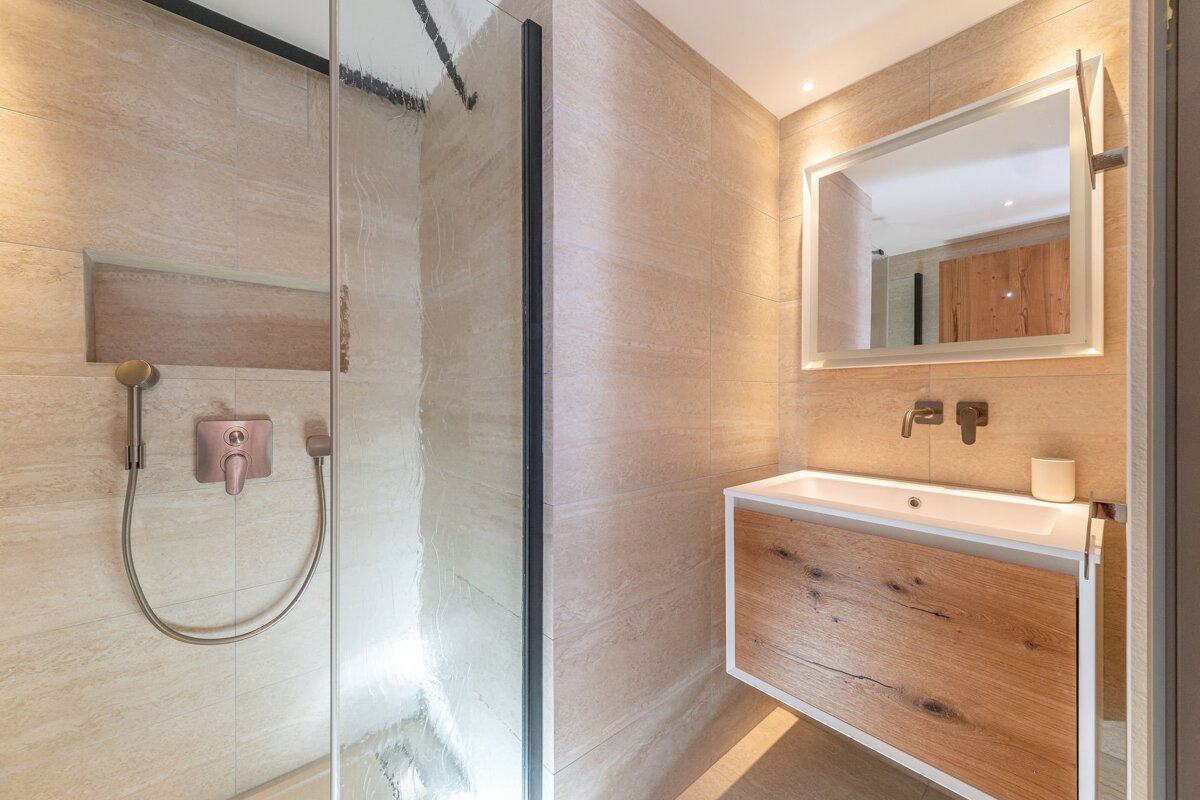 Modern bathroom featuring light beige tiling, a glass shower cabin, and a floating wooden vanity with a framed mirror.