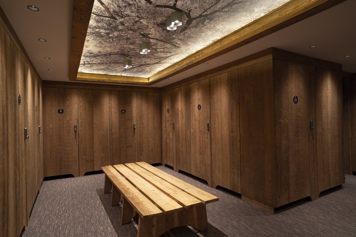 A stylish locker room featuring wooden lockers, a bench, and an illuminated ceiling with a striking tree branch pattern.