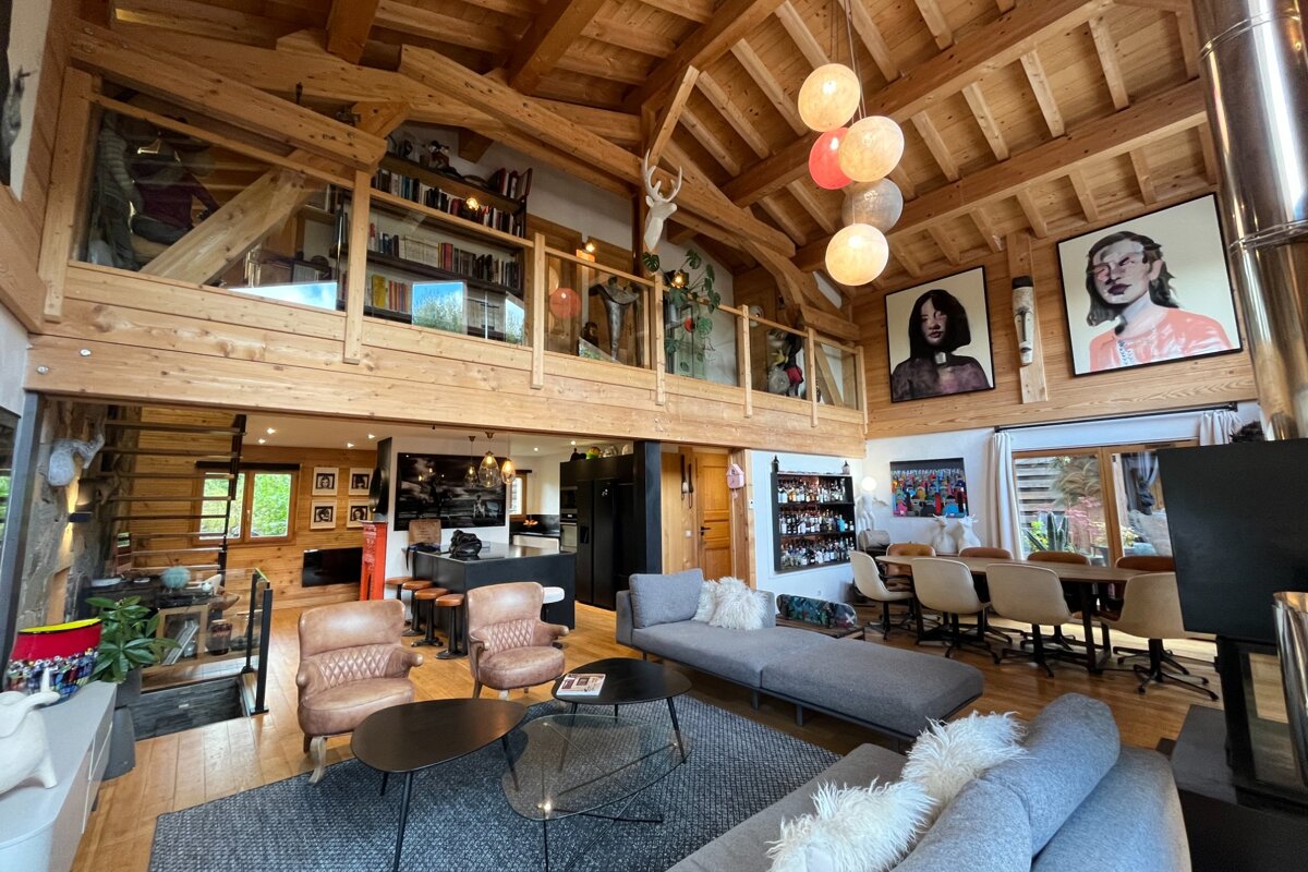 Spacious, modern-rustic living room with exposed wood beams, a loft, eclectic decor, and large portrait artwork.