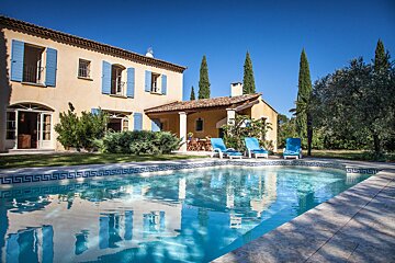 A large house with blue shutters sits next to a large swimming pool