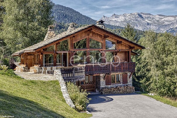A large wooden chalet with mountains in the background