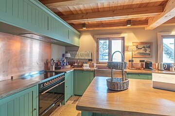 Rustic kitchen with green cabinets, a wooden island, exposed ceiling beams, and a copper backsplash.