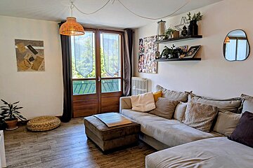 Cozy living room featuring a beige sectional sofa, wooden floors, wall decor, and glass doors opening to a scenic balcony view.