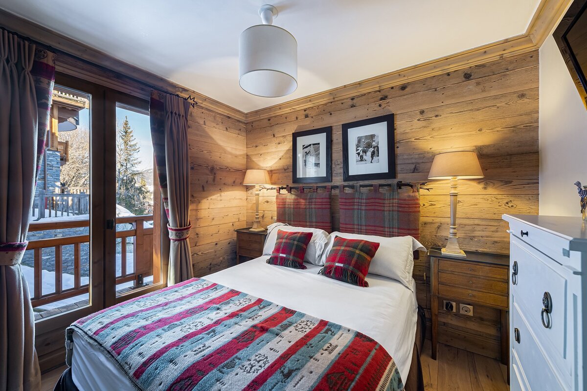 A bedroom with wood paneling and a bed with a plaid headboard