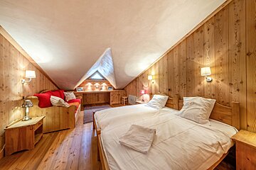 Cozy attic bedroom with wood-paneled walls, a double bed, a red sofa, and a slanted white ceiling.
