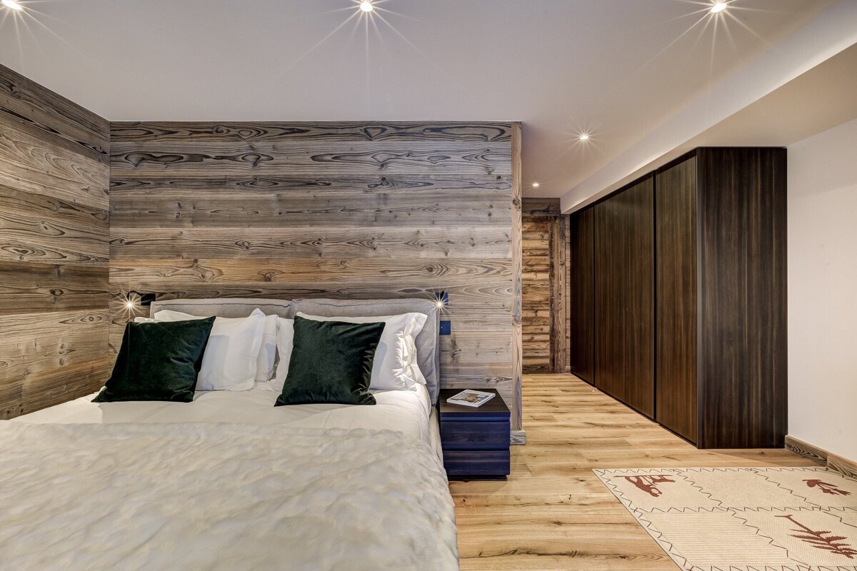 A bedroom with a wooden wall and a bed with green pillows