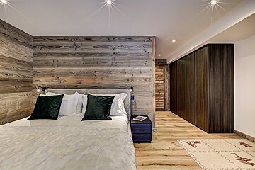 A bedroom with a wooden wall and a bed with green pillows