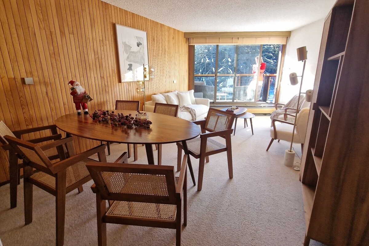 A cozy living/dining room with wood paneling, a festive table, white sofa, and a large window looking out onto a snowy scene.