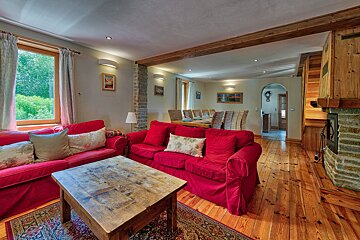 A cozy living room featuring bright red sofas, a rustic wooden coffee table, and hardwood floors. A dining area is in the background, and a fireplace is to the right.