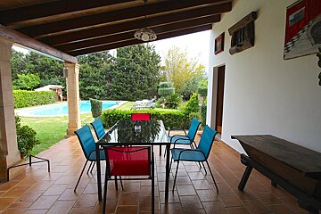 A table and chairs on a patio with a pool in the background