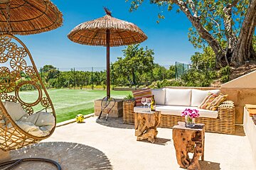 A patio with wicker furniture and umbrellas with a tennis court in the background