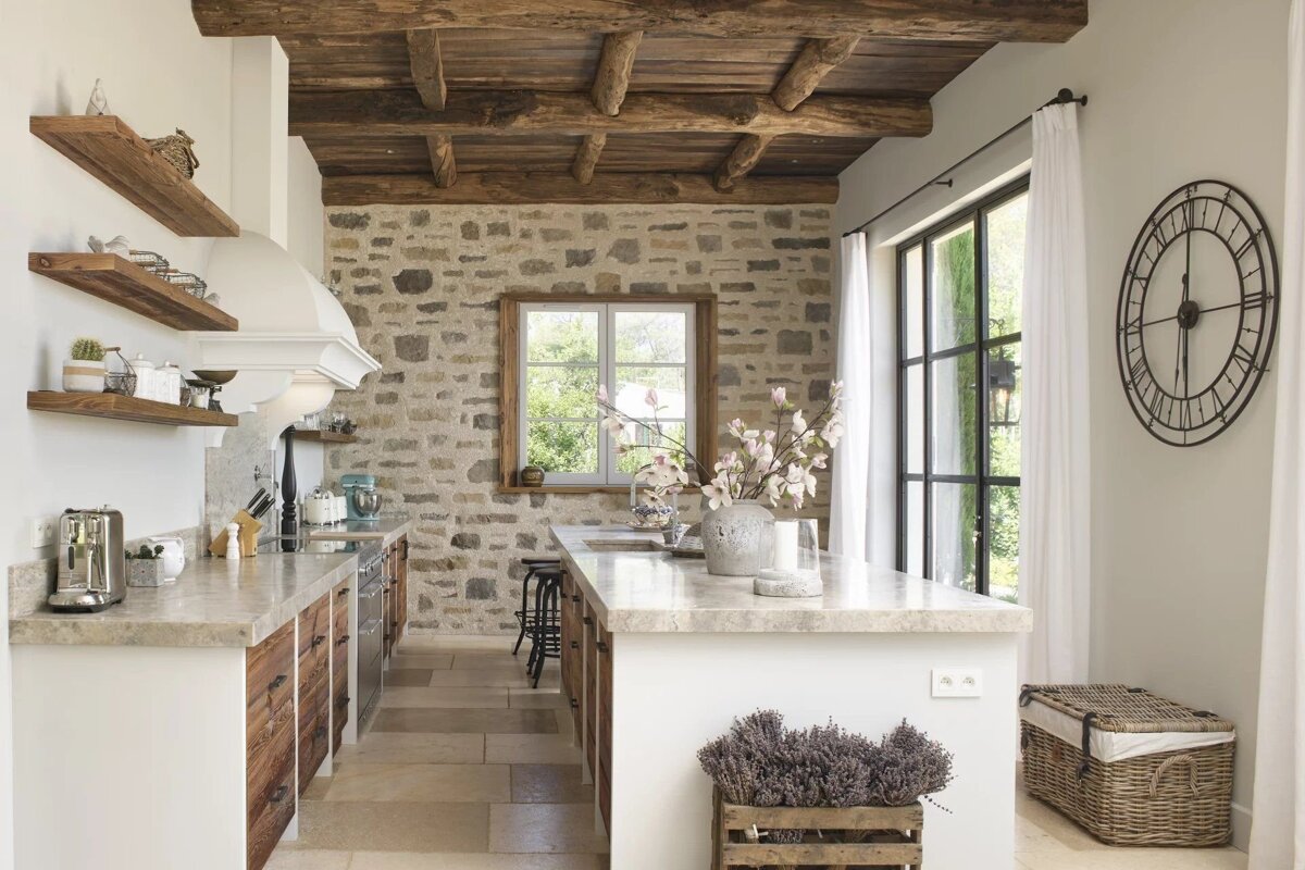 A rustic farmhouse kitchen with exposed wooden ceiling beams, a stone accent wall, marble countertops, and open wood shelves.