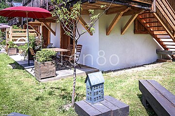 A small house sits on a wooden bench in front of a white building with the number 80 on it