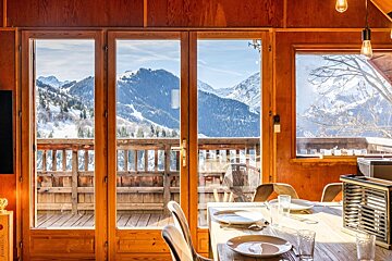 Cozy wooden cabin dining area looking out at a stunning view of snow-covered mountains through large glass doors.