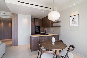 A modern open-plan kitchen and dining area featuring dark wood cabinets, a round dining table, and a large white pendant light.