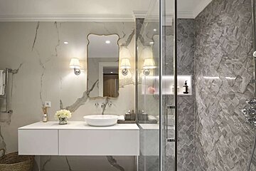 Luxurious bathroom with white marble walls, a floating vanity, ornate mirror, and a modern shower featuring textured grey tiles.