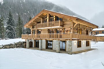 A large wooden house is surrounded by snow and trees