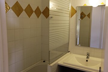 A white tiled bathroom with golden diamond pattern, featuring a bathtub with glass screen, sink, and mirror.