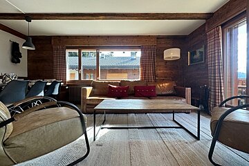 Cozy rustic chalet living room with wood-paneled walls, a leather sofa, two armchairs, and a low wooden coffee table.