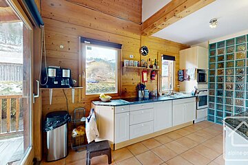 Rustic kitchen with wood walls, white cabinets, tiled floor, and a glass block feature wall. Windows offer outdoor views.