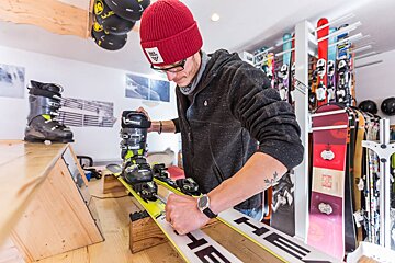 A man wearing a red beanie is working on a pair of skis