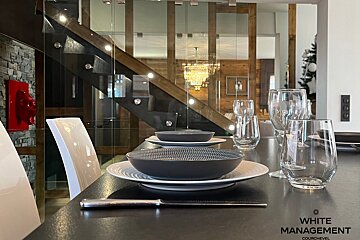 Elegant dining table set with grey bowls and glasses, looking toward a modern wood and glass staircase in a luxury interior.