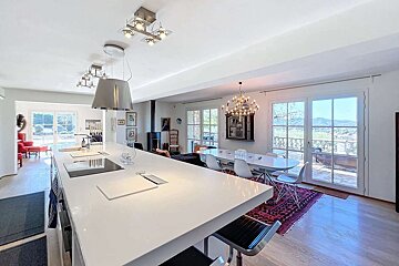 Bright, open-plan kitchen and dining room with a white island, modern decor, and large windows offering a scenic mountain view.