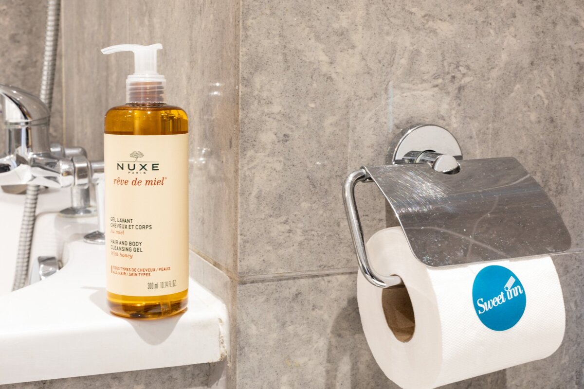 A bottle of nuxe rice de miel next to a roll of toilet paper