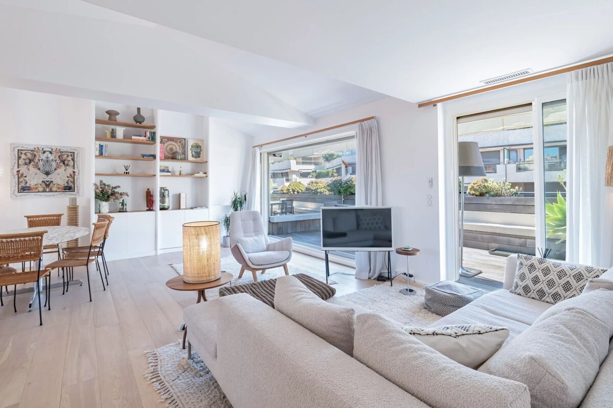 Bright, modern living room with a cream sectional sofa, dining area, built-in shelves, and glass doors opening to a terrace.