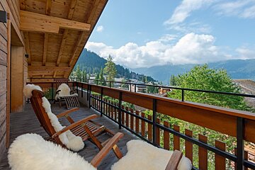 Cozy chalet balcony with sheepskin-covered chairs overlooking a beautiful mountain valley.