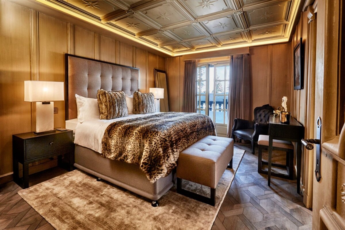 Luxurious wood-paneled bedroom with an ornate ceiling, king-size bed with leopard print, elegant furnishings, and a winter balcony view.