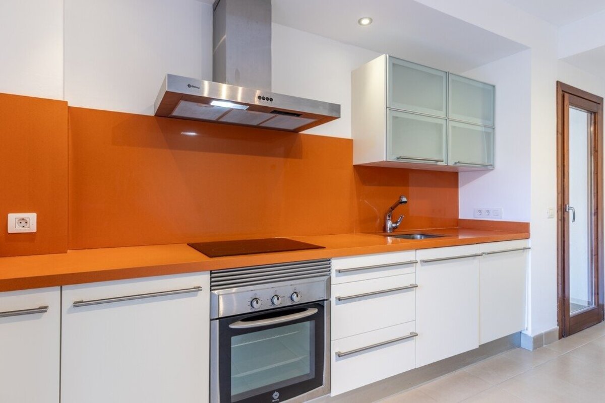 Modern kitchen with bright orange counters & backsplash, white cabinets, and stainless steel appliances including an oven, hob, and hood.