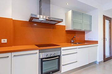 A modern kitchen featuring white cabinets, stainless steel appliances, and a vibrant orange countertop and backsplash.