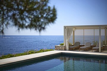 A luxurious pool deck overlooks the ocean, featuring a modern cabana with three lounge chairs.