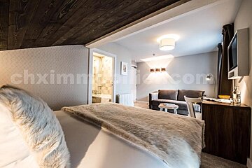 A cozy hotel room with a furry bed, wood-paneled ceiling, separate living area with a sofa, and a glimpse of the bathroom through an open door.