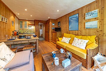 Cozy alpine cabin living room with wood-paneled walls, a bright yellow sofa, wooden coffee table, and dining area in the background.