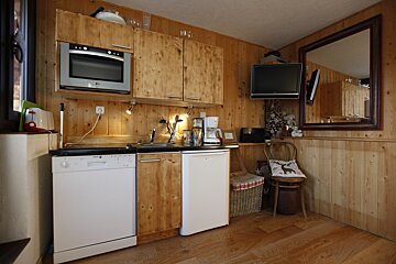 Cozy kitchen with wood paneling, featuring built-in oven, dishwasher, fridge, coffee maker, TV, and a mirror.