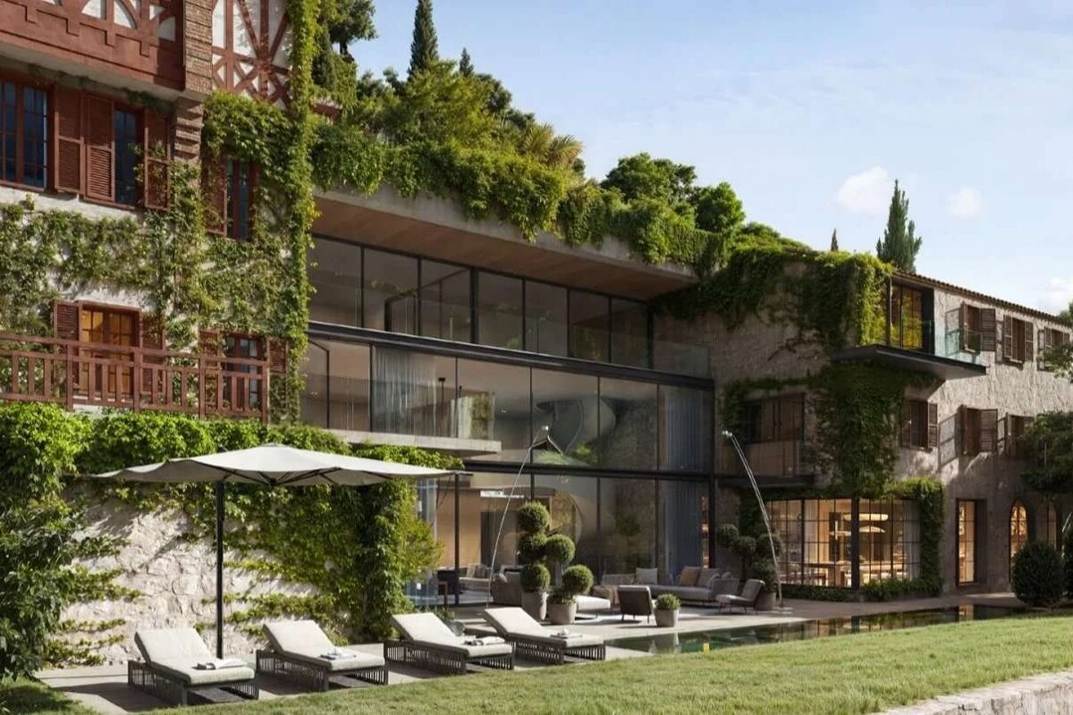 A luxurious building blending modern glass with traditional stone, covered in vines, with an outdoor pool area and loungers.