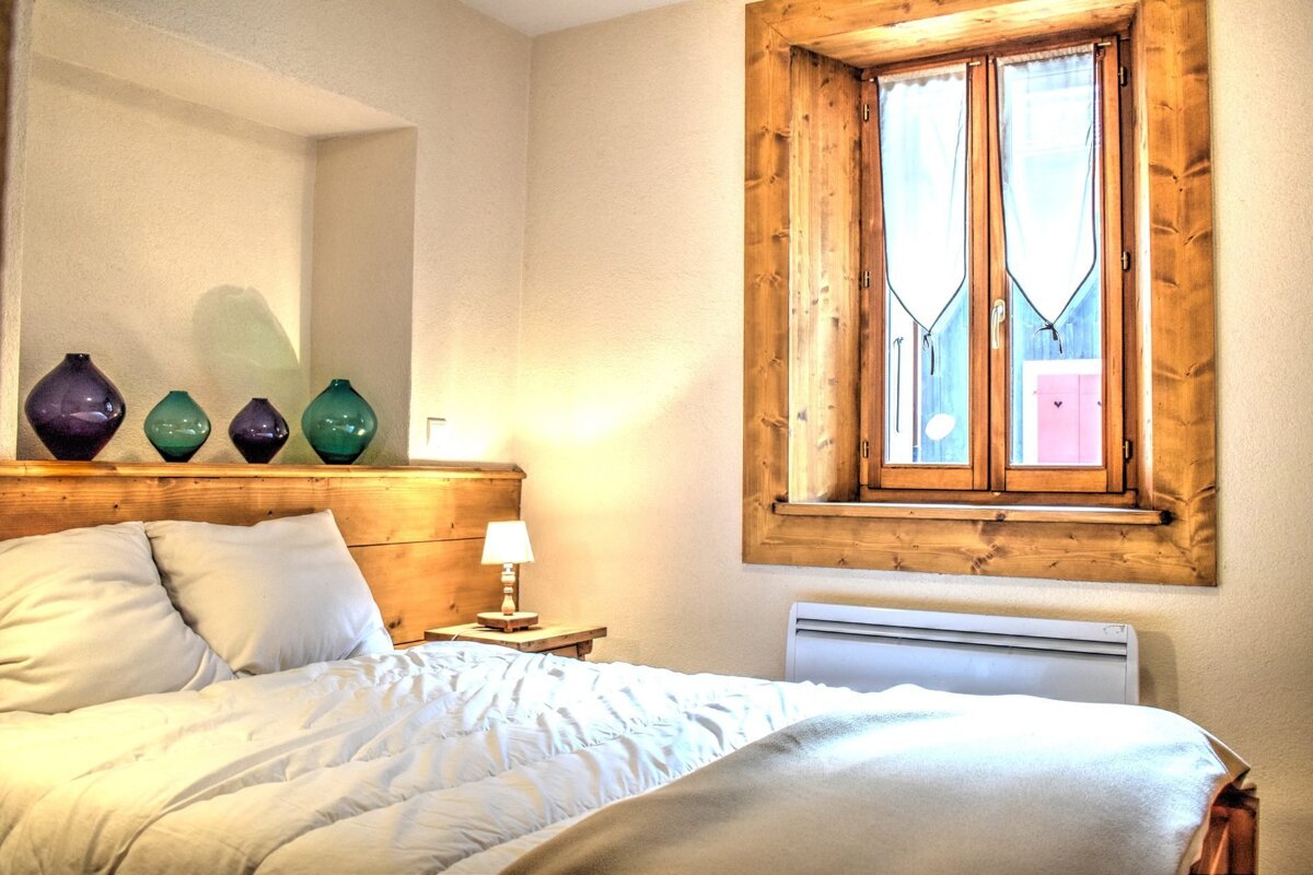 A bedroom with a bed and a window with purple vases on the wall